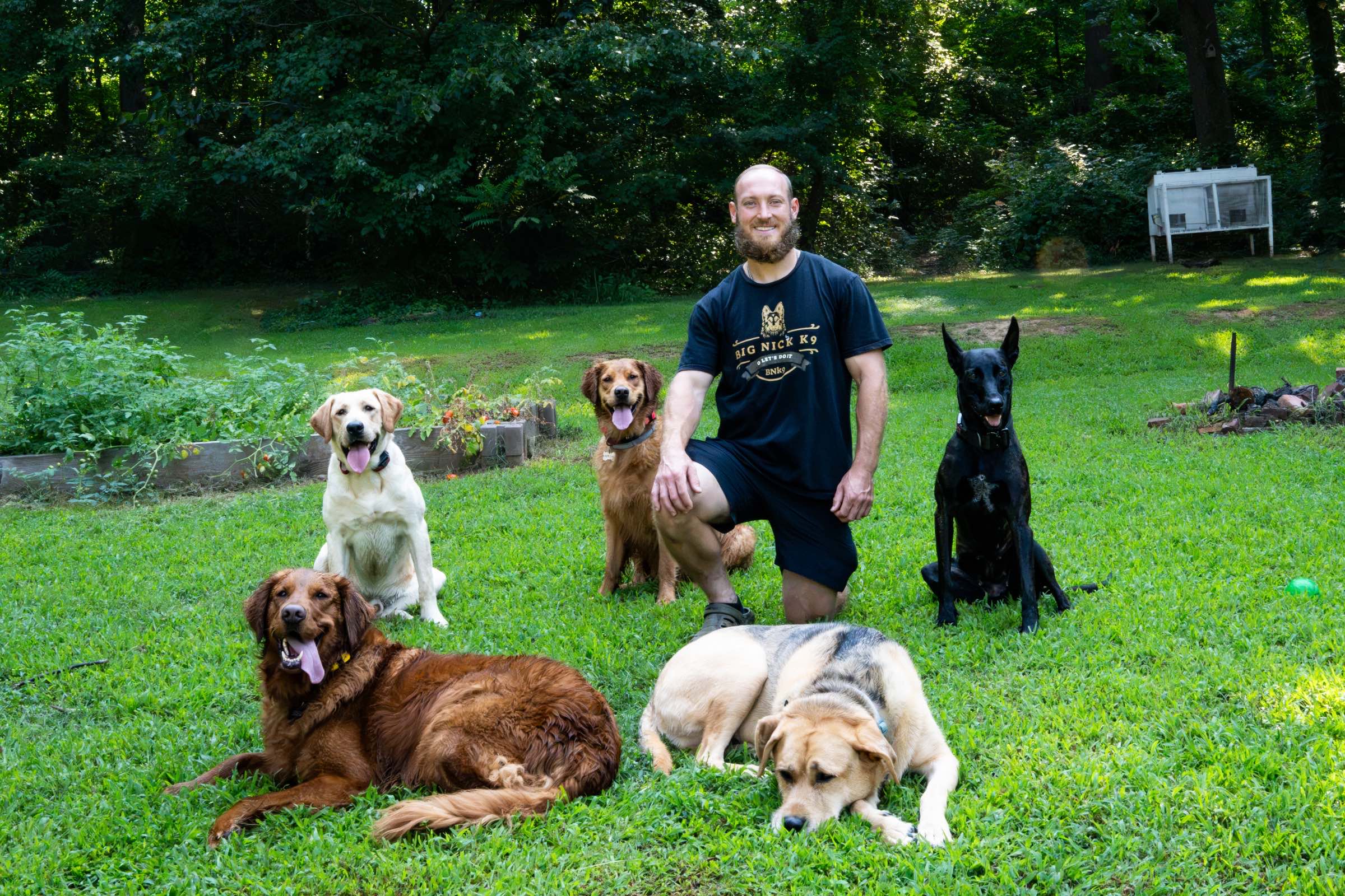 Nick Gallina kneeling in the yard with five dogs holding a stay around him