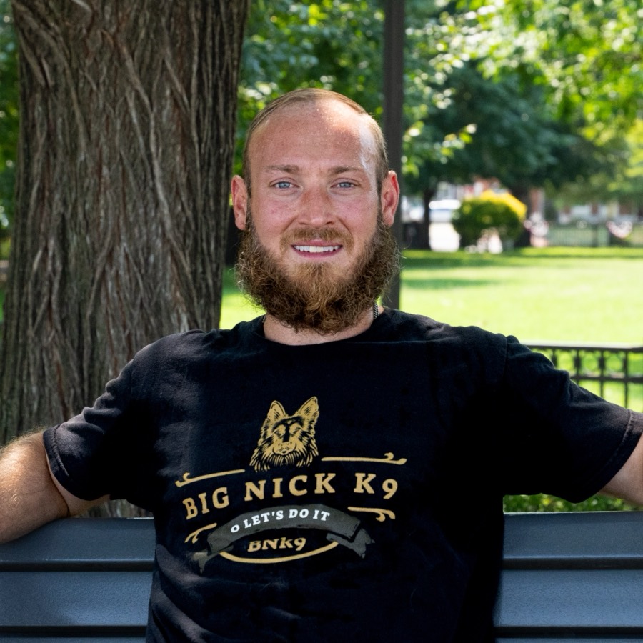 Nick Gallina sitting on a park bench in a Big Nick K9 shirt